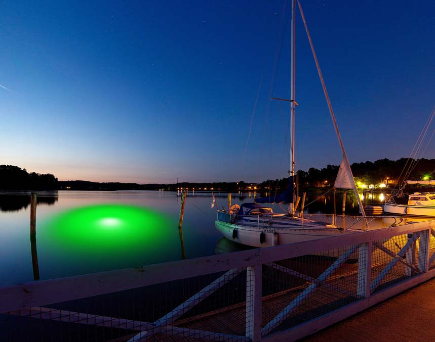 An underwater LED light illuminating the water near a dock with boats