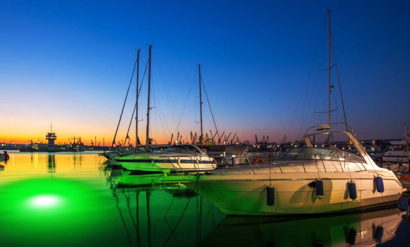 An underwater LED light illuminating the water near a dock with ships