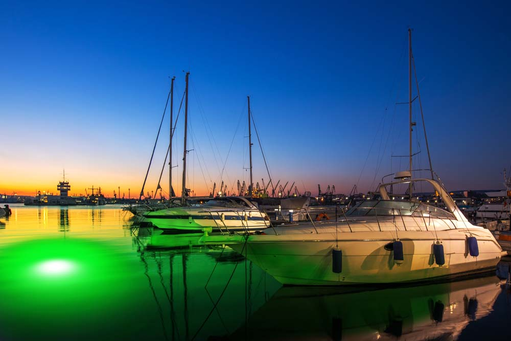 An underwater LED light illuminating the water near a dock with ships