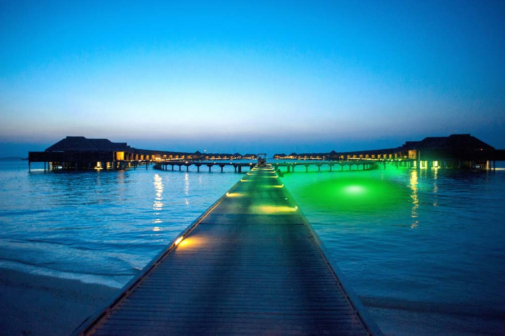 Several beach houses next to the dock with a green underwater LED light.