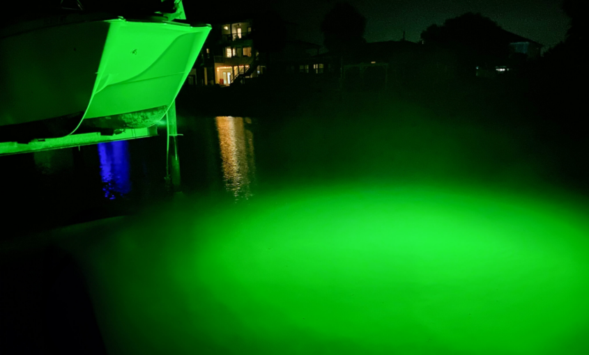 A green light illuminated in the water next to a dock