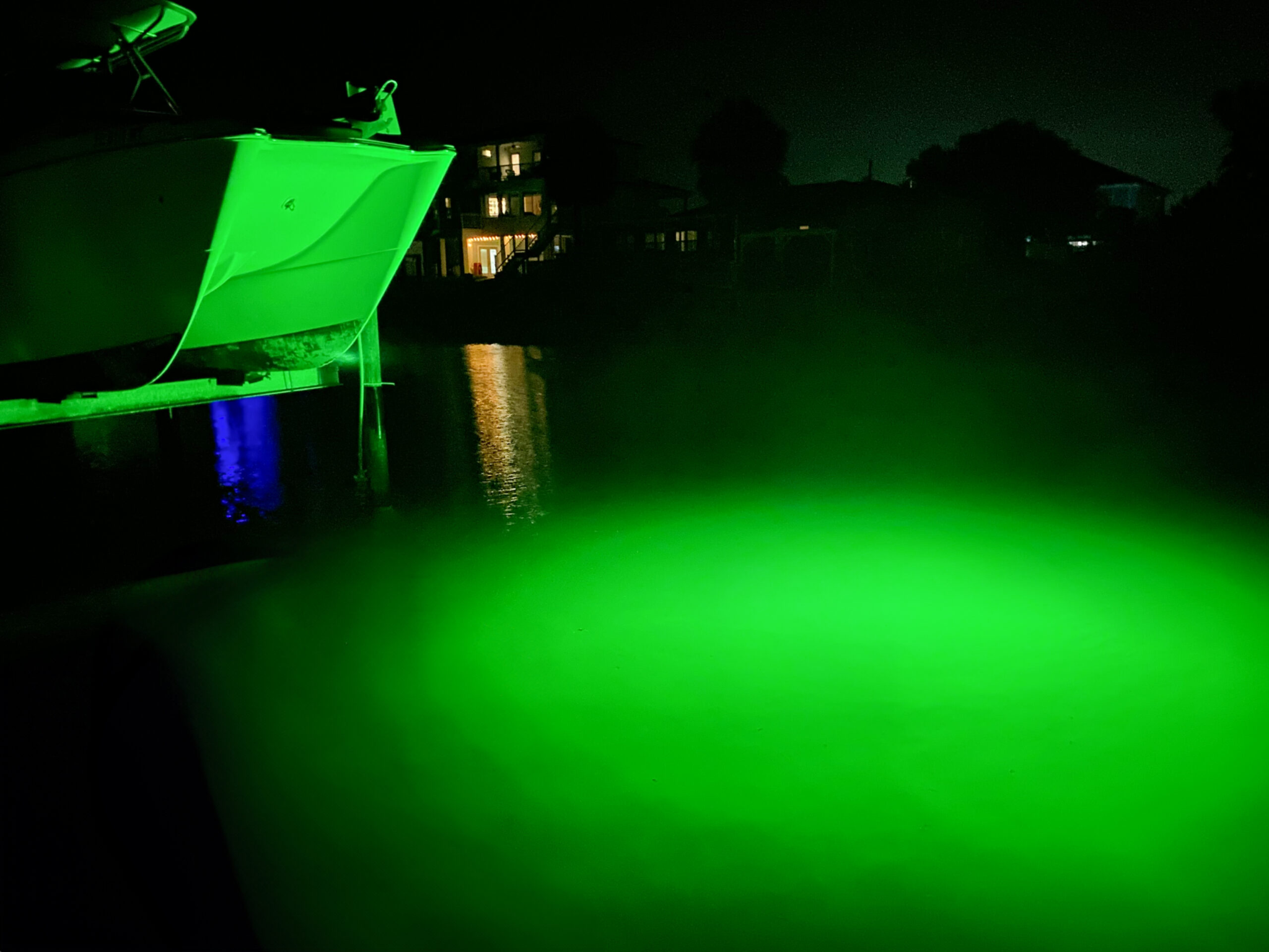 A green light illuminated in the water next to a dock