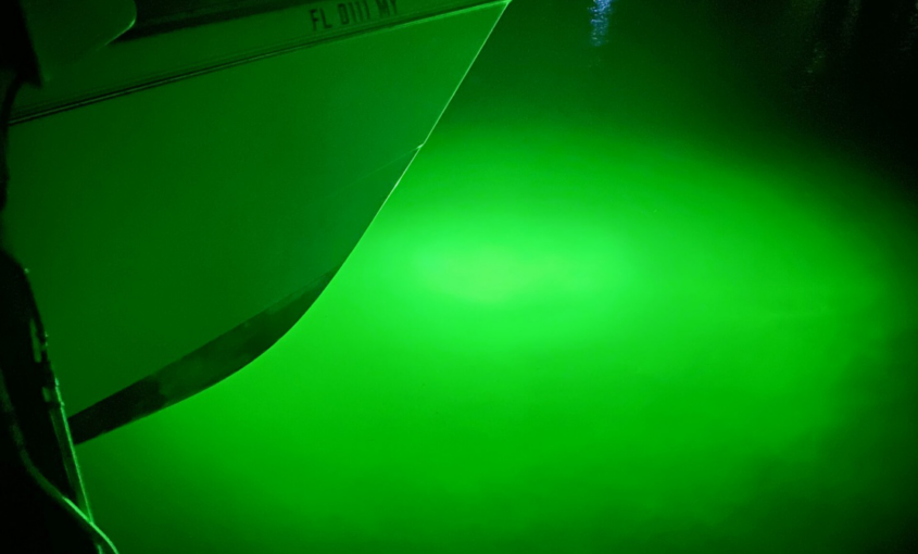 A boat illuminated by green underwater lights