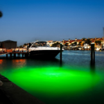 A boat parked next to the dock with a green underwater light.